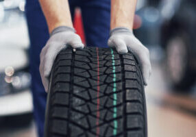 Closeup of mechanic hands pushing a black tire in the workshop.